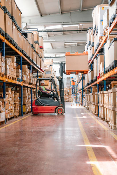 Uniformed Worker Driving and Loading Cardboard Boxes with Forklift Stacker Loader in a Factory Warehouse stock photo