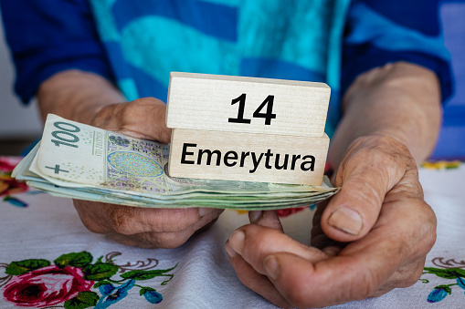 Polish pensioner holds money and wooden blocks with the inscription 