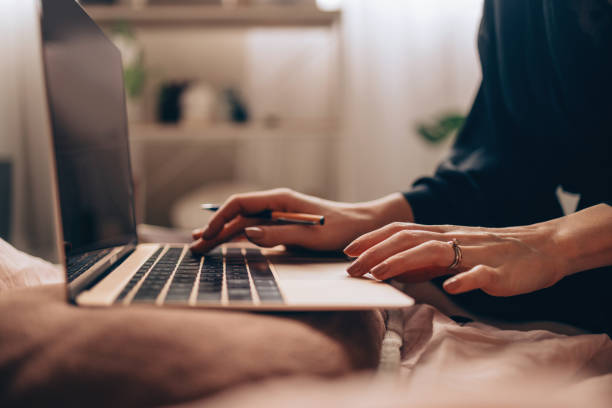 working from home: unrecognizable woman writing a report on her computer while still in bed - one woman only young women people nightie imagens e fotografias de stock