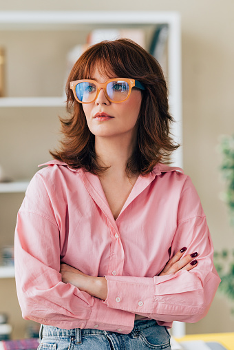 A portrait of a confident businesswoman wearing a pink shirt, standing in her office.
