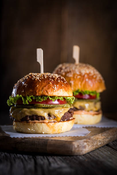 istock Tasty cheeseburger with lettuce, cheddar cheese, tomato and pickles. Burger bun with sesame seeds. Rustic atmosphere. Delicious fast food meal. 1498243665