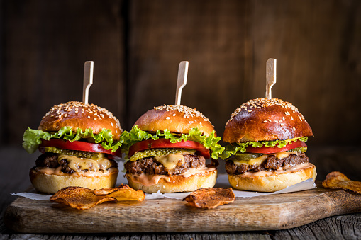 Cheeseburgers on wooden board and table in dark and moody light