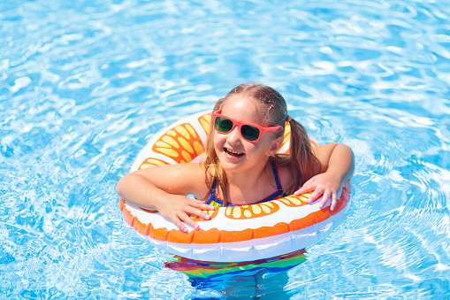 Child in swimming pool floating on toy ring. Kids swim. Colorful yellow float for young kids. Little girl having fun on family summer vacation in tropical resort. Beach and water toys. Sun protection.