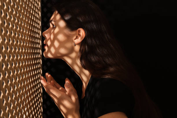 woman talking to priest during confession near wooden partition in booth - confession booth imagens e fotografias de stock