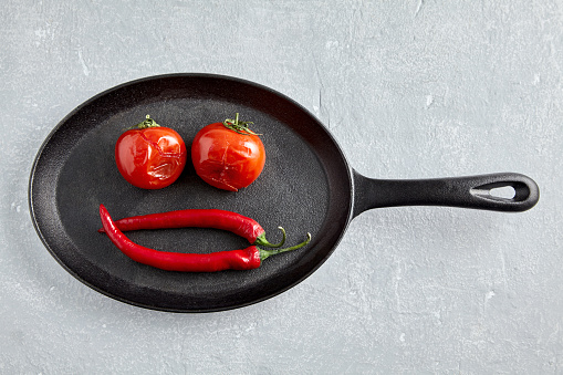 fried grilled baked tomatoes and red hot peppers are laid out in a black pan in the shape of a smiley. top view with copy space