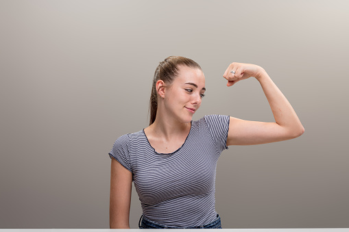 Girl raising her arm and flexing, smiles ironically at her own bicep. Not disheartened, but no expectations of results missed due to lack of exercise. Time to get moving again! Hop hop!