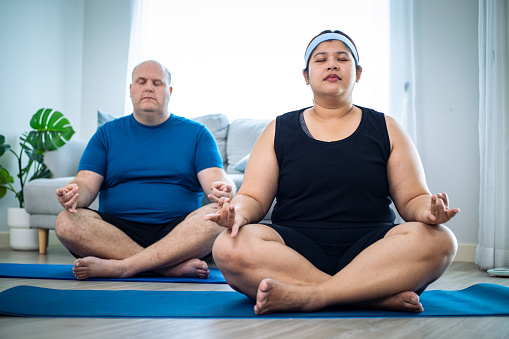 Diversity of fat couple wearing sportswear and doing yoga exercise together while meditating in the studio with blue mat.