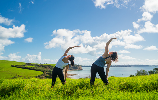 Two women practicing yoga outdoor near river, stretching and exercising.
