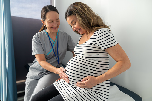 Close up shot of an expectant mother with her hand on her abdominal. Obstetrician is gently pressing on patients abdominal.