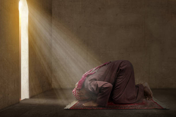 Muslim man with a beard wearing keffiyeh with agal in praying position (salat) on the prayer rug stock photo