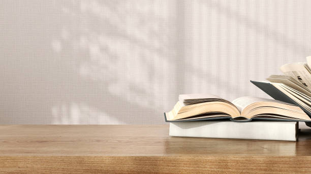 istock Blank brown wooden counter table, open, closed book pile stack in sunlight, leaf shadow on beige texture wallpaper wall 1498296654