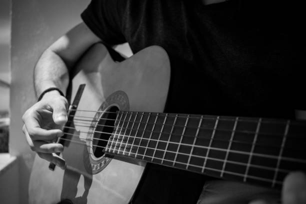 close-up of a man with an acoustic guitar in his hands in grayscale - plucking an instrument imagens e fotografias de stock