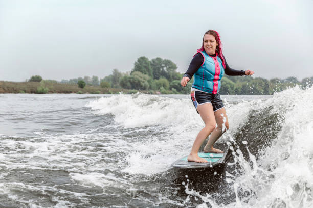 młoda kobieta wakesurfing w dół fal rzeki - wakeboarding motorboating extreme sports waterskiing zdjęcia i obrazy z banku zdjęć