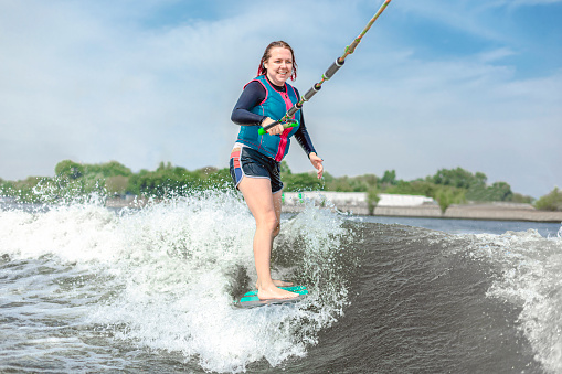 Young girl rides on a wakeboard in the river near forest