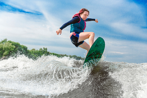 Young girl rides on a wakeboard in the river near forest