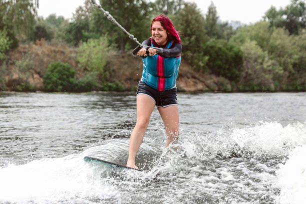 молодая женщина просыпается по волнам реки - wakeboarding motorboating extreme sports waterskiing стоковые фото и изображения