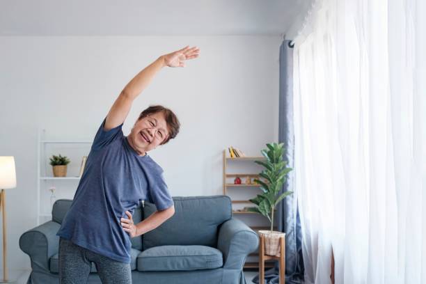 Active mature woman doing stretching exercise in living room at home. Healthy lifestyle and aging concept. Balance in life. Senior woman doing stretching exercise yoga in living room at home. stretching stock pictures, royalty-free photos & images