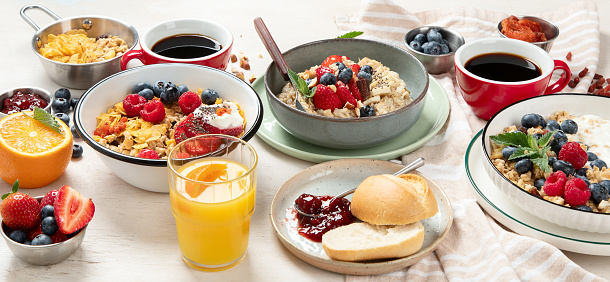 Breakfast food table. Healthy breakfast or brunch set, meal variety with granola, porridge, cornflakes, fresh berries, fruits and various of topping on a white background. Top view. Panorama.