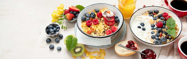 Breakfast food table. Healthy breakfast or brunch set, meal variety with granola, porridge, cornflakes, fresh berries, fruits and various of topping on a white background. Top view. Panorama with copy space.