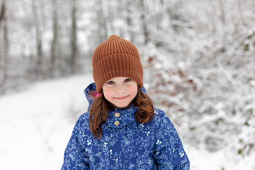Portrait of a little girl in a blue jacket and hat in the winter forest