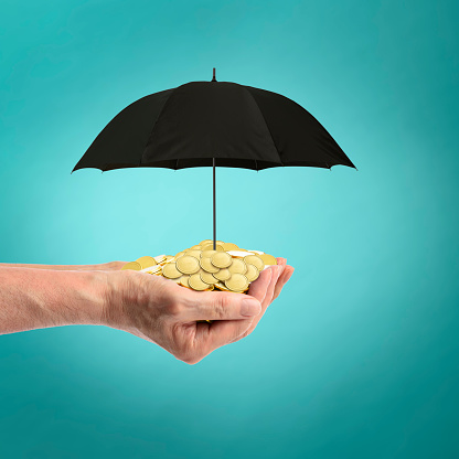 Close-up of gold coins full of both hands under the umbrella against blue background.