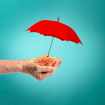 Close-up of gold coins full of both hands under the red umbrella against blue background.