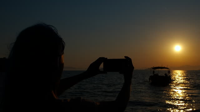 Teen silhouette use smartphone by sea sunset.