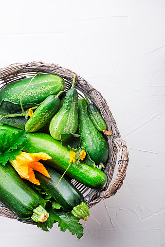 Basket of fresh vegetable crops with fresh zucchini and cucumbers on white background closeup