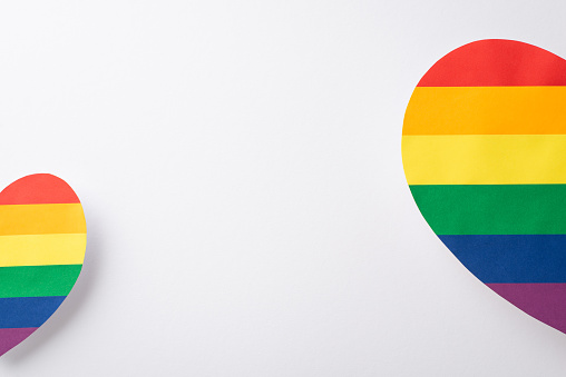 A top view flat lay view of LGBT support items, including two halves of multicolored hearts, laid out on a white backdrop with an empty space for text or advertising