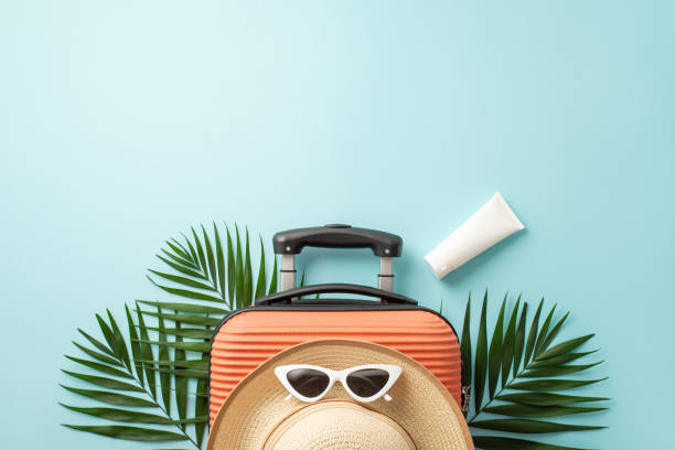 istock Dreamy holiday essentials. Orange suitcase seen from top view, beach essentials, stylish sunglasses, hat, sunscreen bottle and palm leaves on a pastel blue background, perfect for text or advertising 1498323785