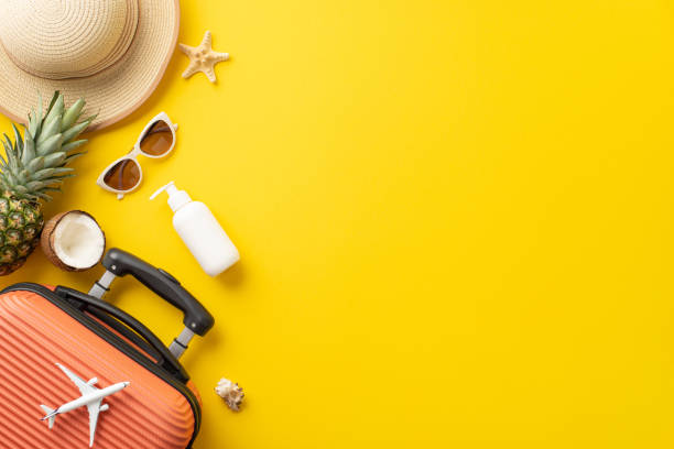 istock Longing for vacation. Top view setup displaying suitcase, small airplane model, beach gear, sunglasses, hat, sunscreen, starfish, juicy fruits on yellow backdrop. Empty space provided for text or ads 1498324362