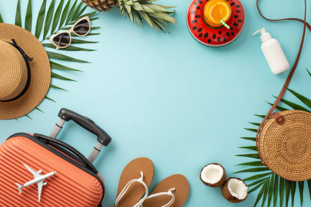 istock Summer party theme. Top view suitcase, tiny plane model, pool accessories, glasses, hat, sunscreen, flip-flops, rubber ring, cocktail, fruits, palm leaves on light blue backdrop, frame for text or ad 1498324379