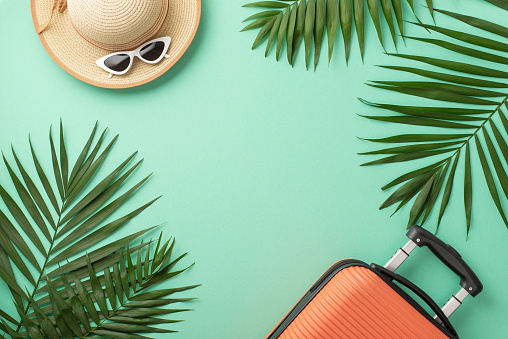 Escape to paradise against a stunning teal backdrop, showcasing a top view of a suitcase, beach gear, sunglasses, sunhat, and palm leaves. Ideal for travel ads