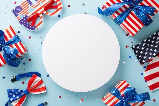Celebration of Independence Day in the United States. Top view of symbolic party ornaments: confetti, party glasses, tie, bow-tie, gift boxes, pastel blue background with empty circle for text or ad