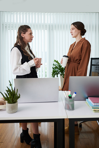 Vertical image of businesswomen drinking coffee and talking during coffee break in office