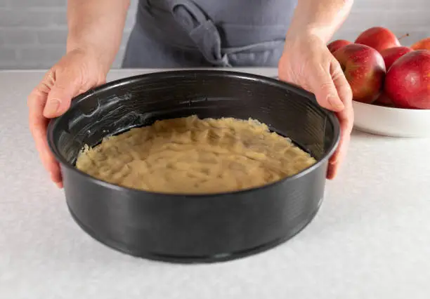 Making a cake. Woman holding a round baking pan with fresh short crust pastry on kitchen counter. Closeup, front view