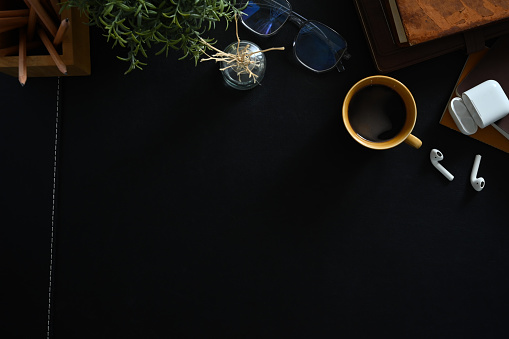 Above view of stylish workplace with cup of coffee, glasses notebook and earphones on black leather background.