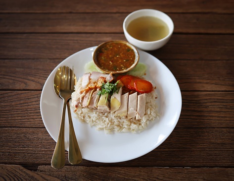 Khao Mun Gai, Thai food, rice steamed with chicken soup serve with chicken, soup and sauce on dark tone texture background,
gold spoon