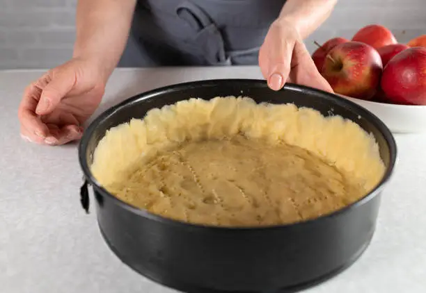 Fresh short crust pastry poked in a round baking pan on kitchen counter. Holding by womans hands