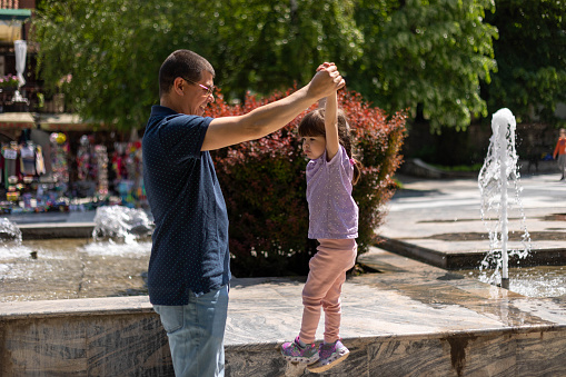 A man is having a great time with his daughter. She is holding her daughter's hands and smiling at her.