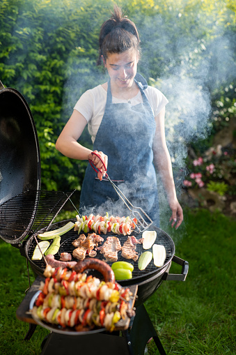 Woman preparing delicious meal at the grill barbeque in the back yard.