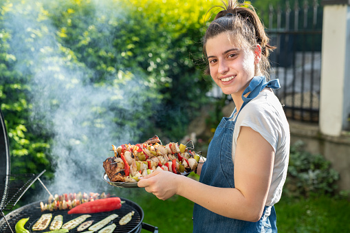 Portrait of smiling woman preparing food on a barbeque in the back yard on a sunny day.