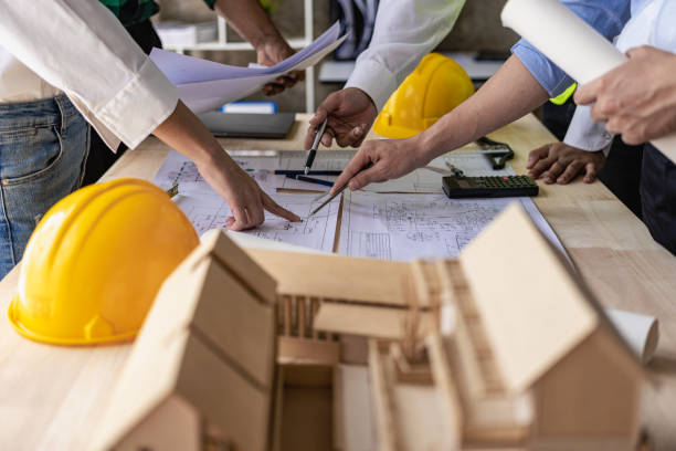 istock Two engineers wearing yellow clothes working and discussing white grand plan document Two colleagues discussing data and laptop with architectural project at construction site at desk in office 1498342750
