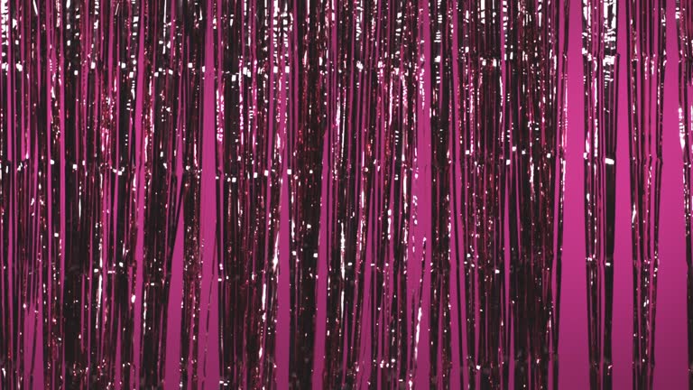 Shiny tinsel curtain flowing in the air against pink colored background