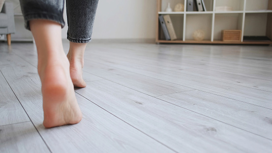 Floor heating. Home barefoot. Unrecognizable woman feet walking on warm laminated wood panels modern flat interior with copy space.