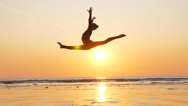 Beautiful shot of young athlete do split in jump, vibrant sea sunset