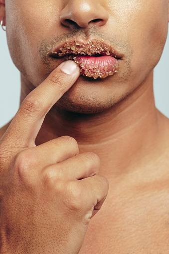 Young man exfoliating his lips with a cleansing lip scrub, part of his grooming and self-care routine. Man applying hydrating ingredients to make his lips more healthy, soft and smooth.