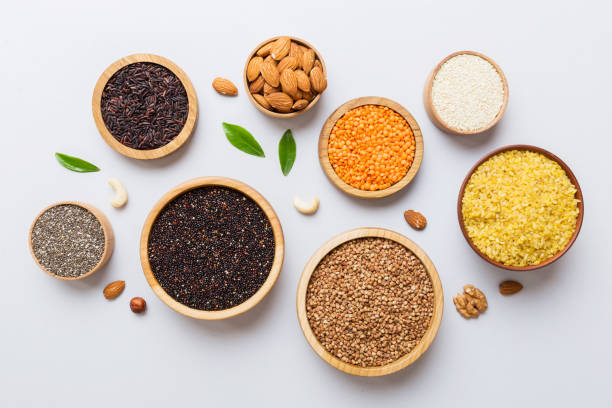 varios superalimentos en tazón pequeño sobre fondo de color. superalimentos como arroz, chía, quinoa, lentejas, nueces, semillas de sésamo, almendras. espacio de copia de vista superior - quinoa sesame chia flax seed fotografías e imágenes de stock