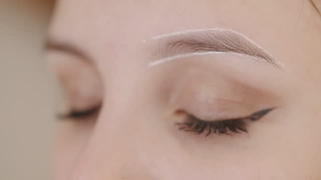 Master applies white markings to correct shape of eyebrows with a special brush.