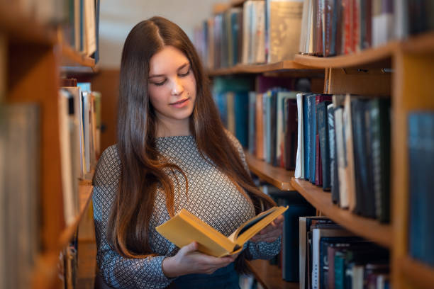 istock Young student girl reading a book in library 1498371038